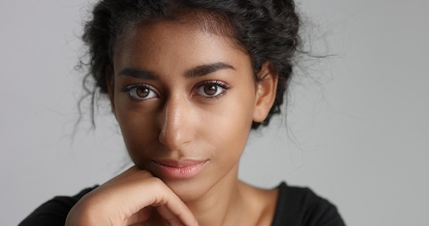 Free photo young girl with perfect light brown skin and beautiful curly black hair smiling at the camera in studio