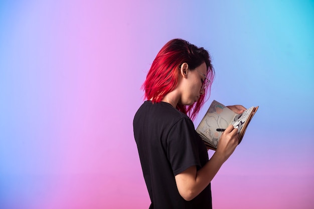 Free photo young girl with pink hairs holding a sketchbook and looking at.