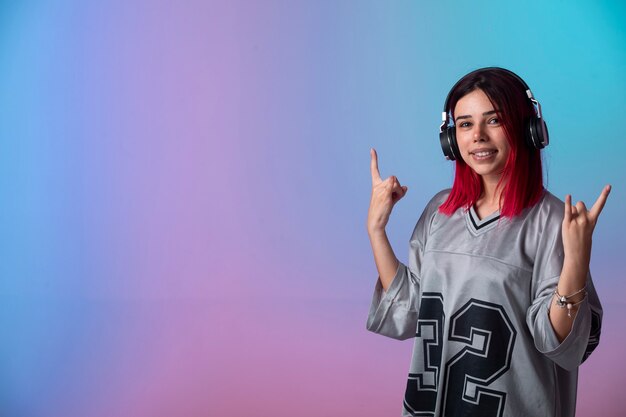 Young girl with pink hairs looks positive and wearing headphones.