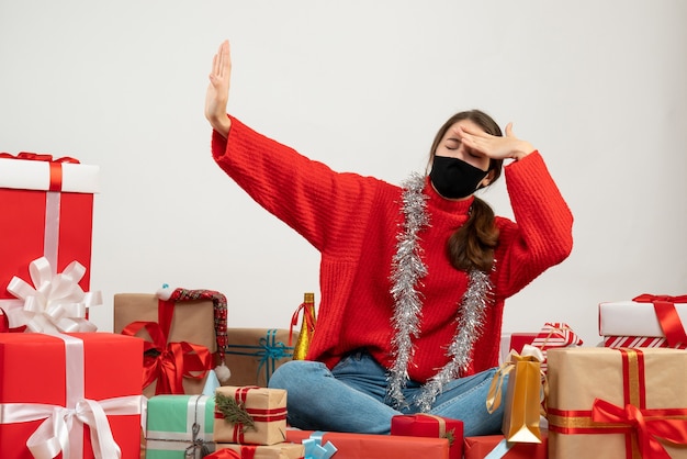 young girl with red sweater and black mask blocking the light sitting around presents on white