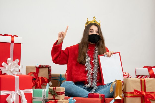 young girl with red sweater sitting around presents with black mask on white