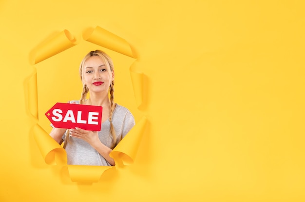 Young girl with sale inscription sign on a torn yellow background fashion shopping indoor