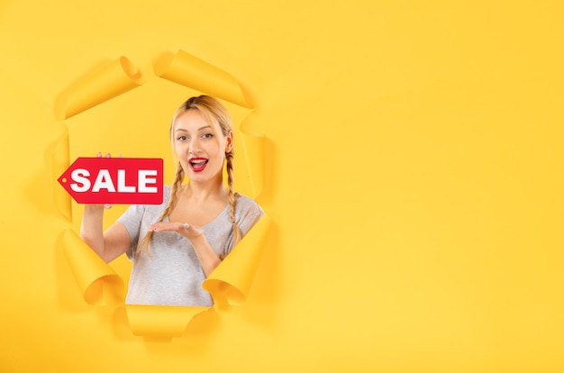 Young girl with sale inscription sign on a torn yellow paper background indoor facial shopping