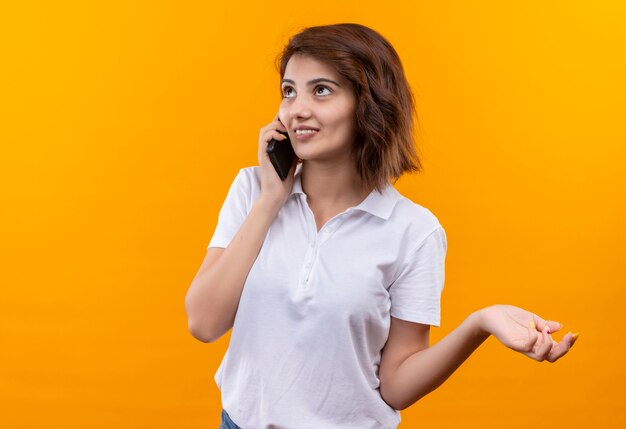 Young girl with short hair wearing white polo shirt smiling while talking on mobile phone