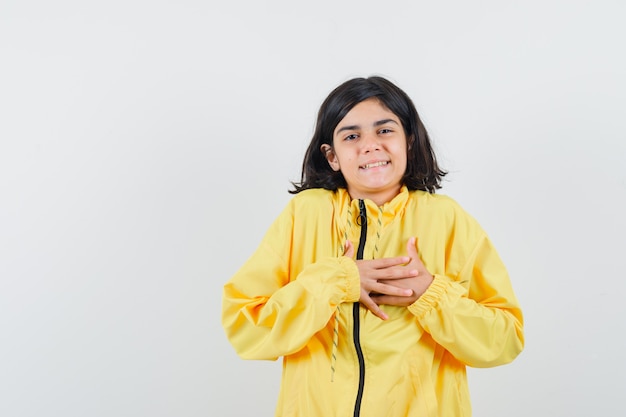 Young girl in yellow bomber jacket resting hands on chest and looking happy