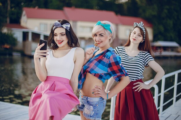 Young girls posing on a white railing and one looking at her mobile phone