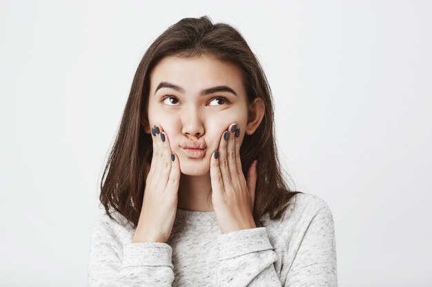 young gorgeous brunette squeezing face with hands, looking up with clueless doubtful expression.