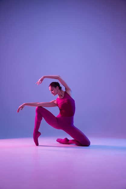 Young and graceful ballet dancer isolated on purple studio background in neon light