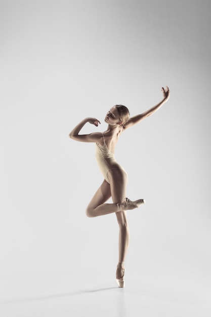 Free Photo young graceful female ballet dancer or classic ballerina dancing on white studio. caucasian model on pointe shoes