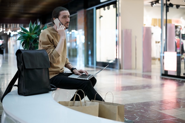 Free photo young guy calls to a friend to tell about sales in shopping center