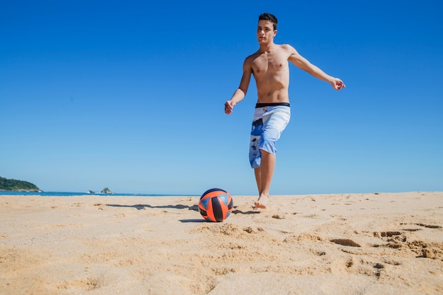 Young guy playing football on the beach