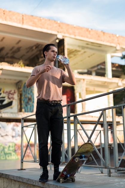 Free photo young guy posing with skateboard and bottle of water