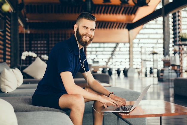 young guy with a beard works in a cafe, freelancer uses a laptop, does a project