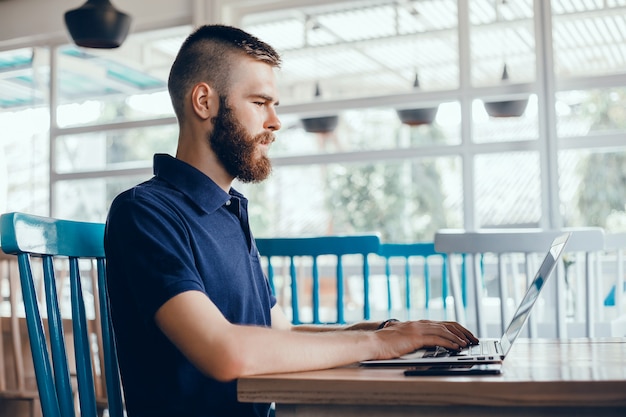 young guy with a beard works in a cafe, freelancer uses a laptop, does a project