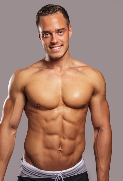 Free photo young guy with great body anatomy in black swim shorts possing in studio. light grey background.