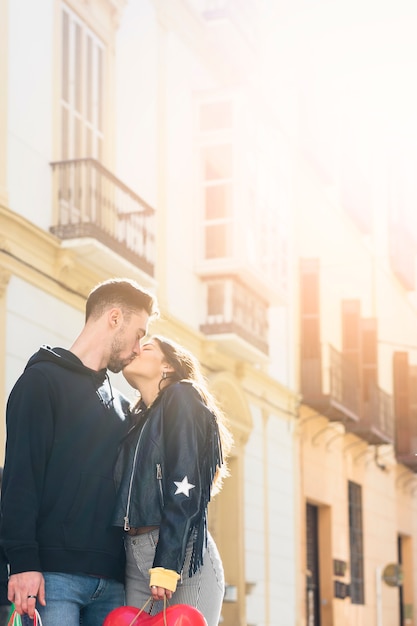 Free Photo young guy with packets kissing lady near building