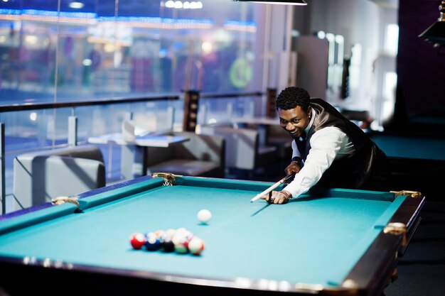 Young handsome african man wearing white shirt black vest and bow tie play pool billiard