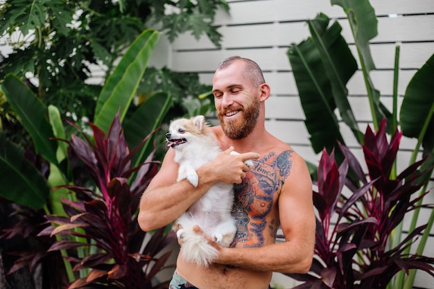 Free Photo young handsome bearded brutal tattooed happy man holds pomeranian spitz playing with lovely pet