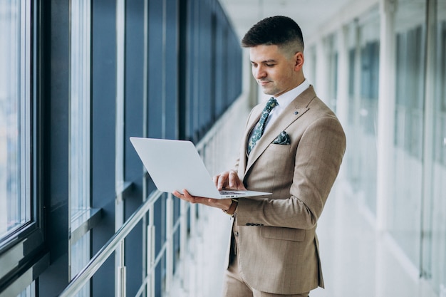 Free photo young handsome business man standing with laptop at the office