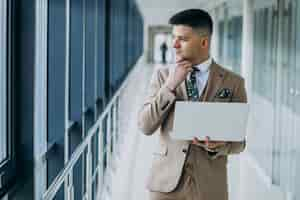 Free photo young handsome business man standing with laptop at the office