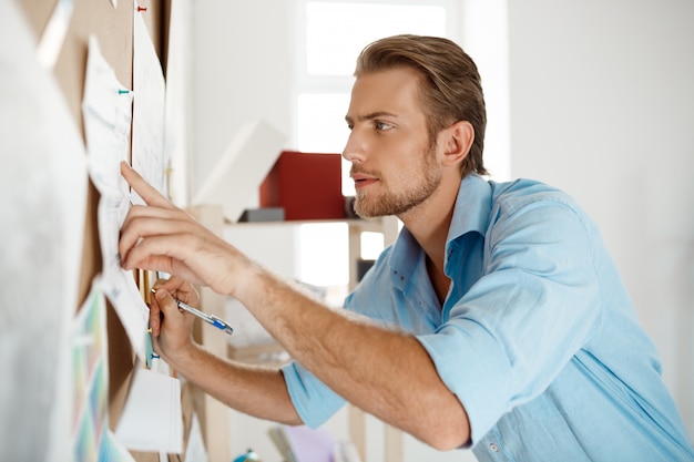 Free Photo young handsome businessman pointing finger and writing at the paper pinned to corkboard.