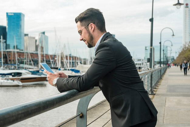 Young handsome businessman standing near the lake using smart phone