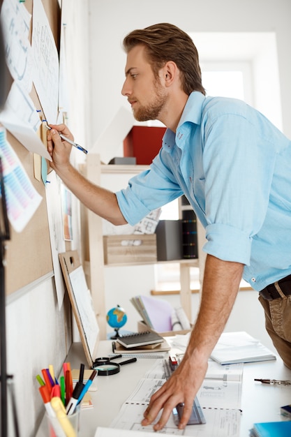 Free photo young handsome businessman writing at the paper pinned to corkboard.