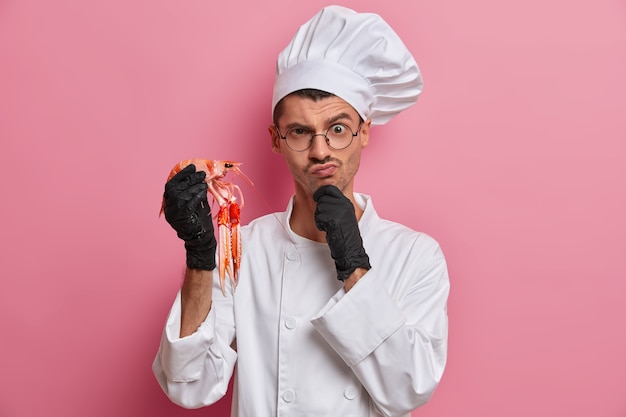 Free photo young handsome chef holding uncooked crayfish isolated