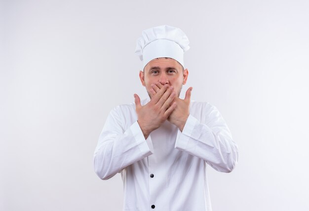 Young handsome cook in chef uniform closing mouth with hands isolated on white space 