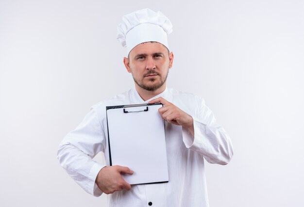 Young handsome cook in chef uniform holding clipboard looking  on isolated white space