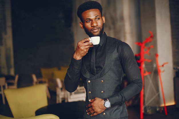 A young and handsome dark-skinned boy in a black suit standing in a cafe