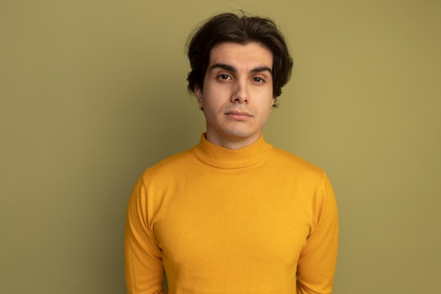 Young handsome guy looking at camera wearing yellow turtleneck sweater isolated on olive green wall