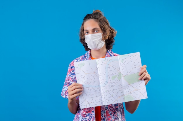 Free photo young handsome guy wearing facial protective mask showing map with serious confident expression on face standing