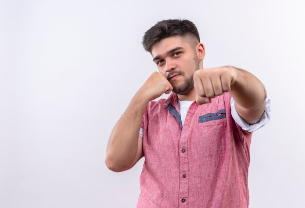 Young handsome guy wearing pink polo shirt shows boxing standing over white wall