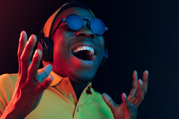 The young handsome happy hipster man listening music with headphones at black  with neon lights