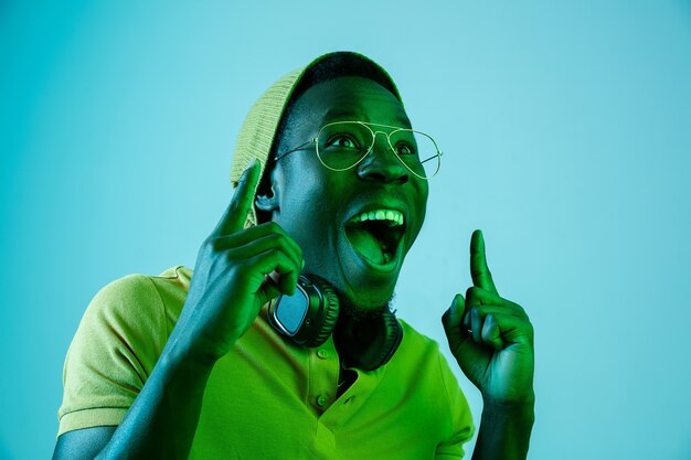 The young handsome happy surprised hipster man listening music with headphones at studio with neon lights. Disco, night club, hip hop style, positive emotions, face expression, dancing concept