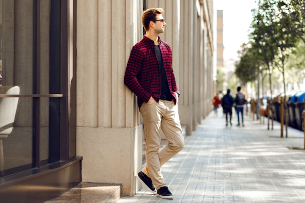 Young handsome hipster man posing on European street, sunny warm toned colors, casual trendy clothes, traveling mood.