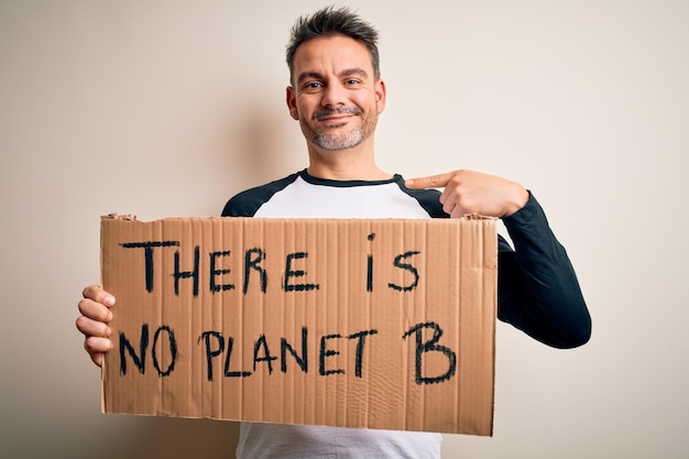 Young handsome man asking for environment holding banner with planet message with surprise face pointing finger to himself