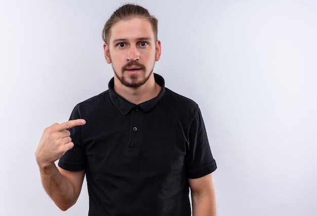 Young handsome man in black polo shirt looking scared pointing to himself standing over white background