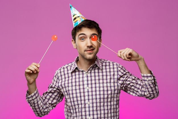 Free photo young handsome man celebrating birthday party over purple wall.