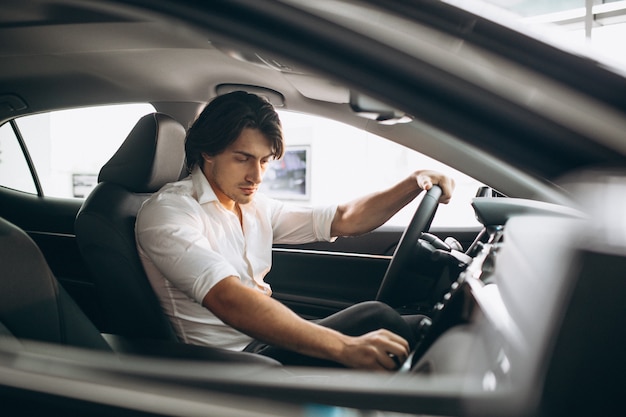 Young handsome man choosing a car in a car showroom