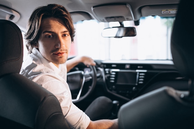 Young handsome man choosing a car in a car showroom