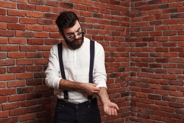 Young handsome man correcting shirt on brick wall.