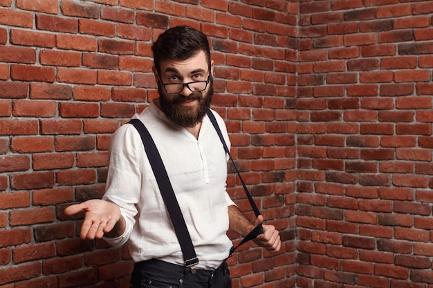 Free photo young handsome man in glasses gesturing on brick wall.