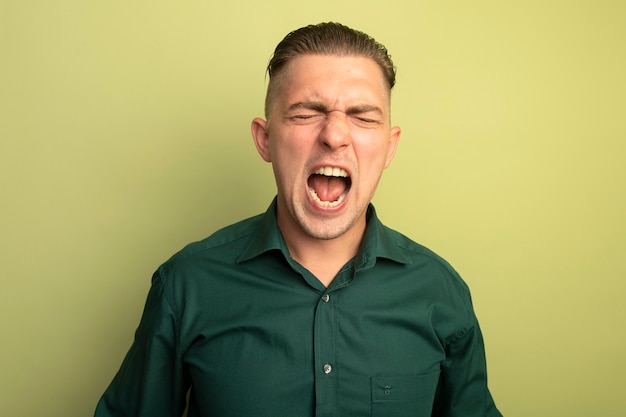 Free photo young handsome man in green shirt shouting with aggressive expression irritated and angry