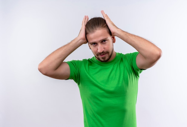 Free photo young handsome man in green t-shirt looking confident touching his perfect hair standing over white background