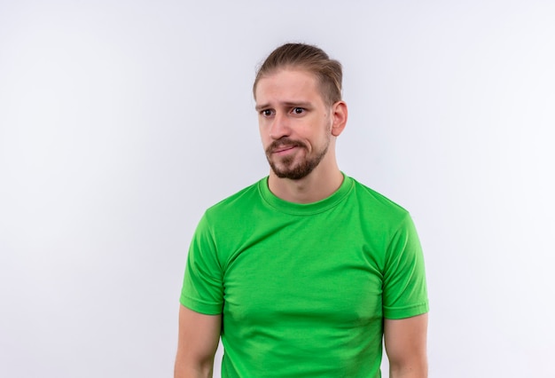 Free photo young handsome man in green t-shirt looking confused and very anxious standing over white background