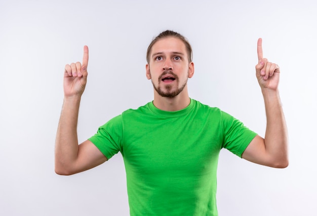 Free photo young handsome man in green t-shirt pointing fingers up looking confident having great idea standing over white background