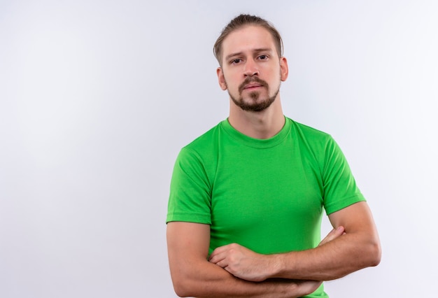 Free photo young handsome man in green t-shirt standing with arms crossed looking at camera with serious face over white background