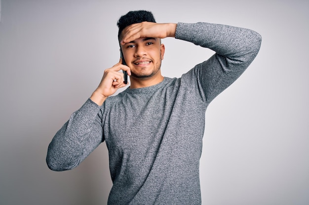 Young handsome man having conversation talking on the smartphone over white background stressed with hand on head shocked with shame and surprise face angry and frustrated Fear and upset for mistake